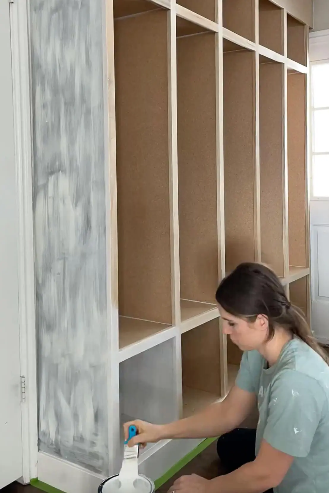 A DIYer applying white primer to a built-in storage unit, prepping the surface for a smooth and durable paint finish.